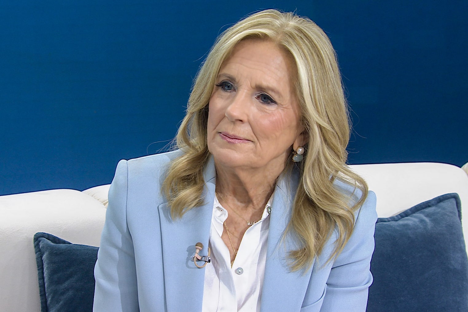 Jill Biden seated on a white couch in front of a blue wall