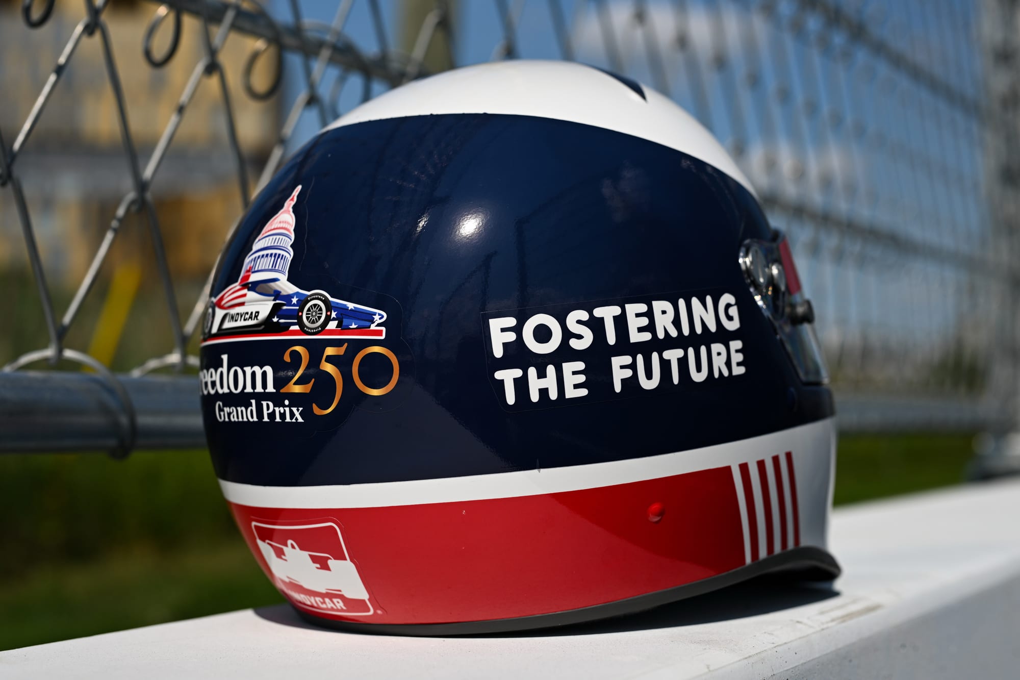 A red, white, and blue racing helmet with text that reads: "Freedom 250 Grand Prix" and "Fostering the Future"